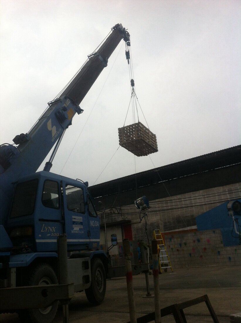 ลังไม้ห้อยอยู่กับตะขอเครนขนาดเล็กของ BIG MACHINE TRADING ระหว่างงานจัดฉากกองถ่ายโฆษณาเครื่องดื่มเกลือแร่