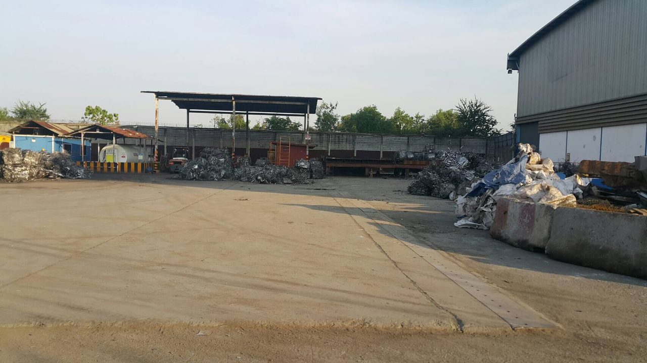 พื้นที่โรงงานรีไซเคิลโลหะขนาดใหญ่ มีโรงเก็บและกองเศษอลูมิเนียมหลายจุดรอบพื้นที่ทำงาน