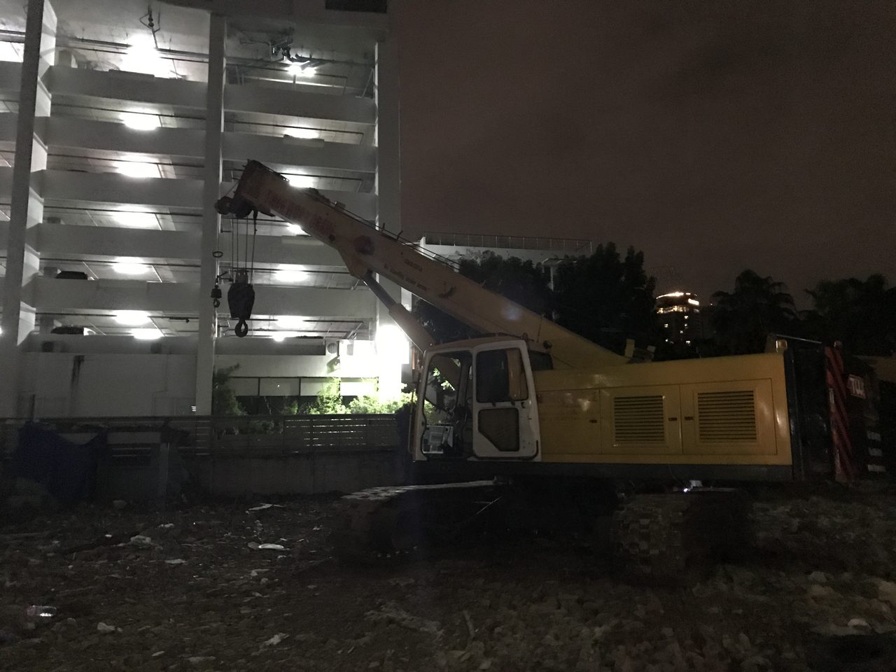 เครนตีนตะขาบ BIG MACHINE TRADING ยืนทำงานกลางคืนใกล้อาคารจอดรถที่ไซต์งาน ASAI Hotel