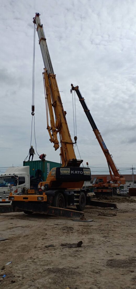 เครนล้อยาง KATO ของ BIG MACHINE TRADING ทำงานร่วมกับเครนอีกคันยกตู้คอนเทนเนอร์ที่ไซต์ก่อสร้างโรงงานนิคมบางปู