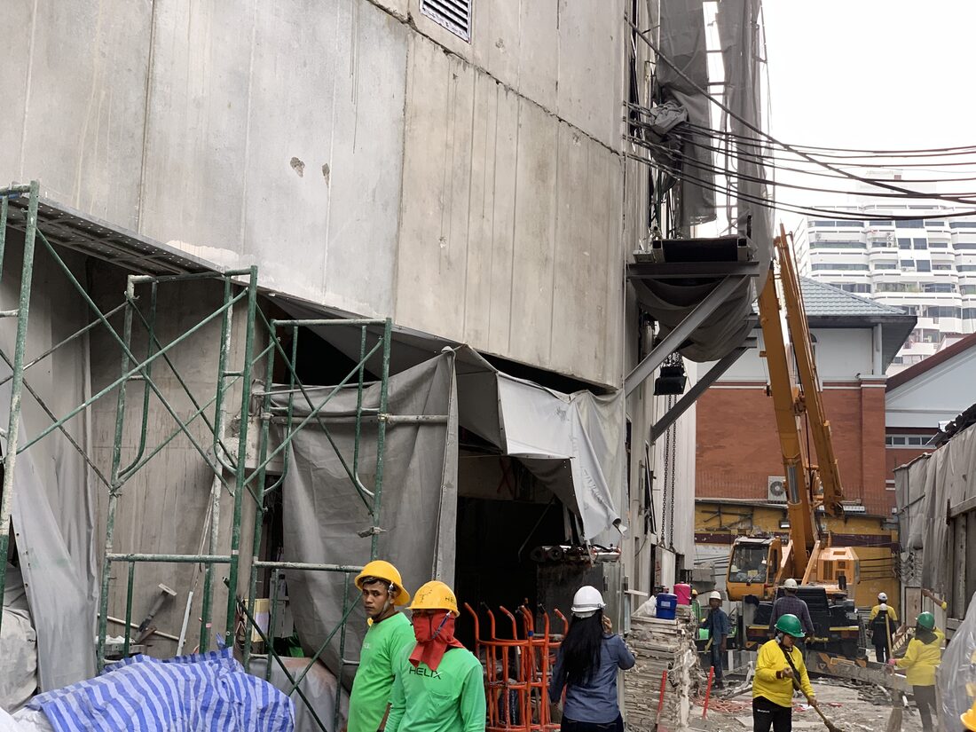 ทีมงานสวมหมวกนิรภัยที่หน้างาน IDEO Q Victory เตรียมประสานงานกับเครนล้อยาง BIG MACHINE TRADING ที่ทำงานในตรอกแคบข้างอาคาร