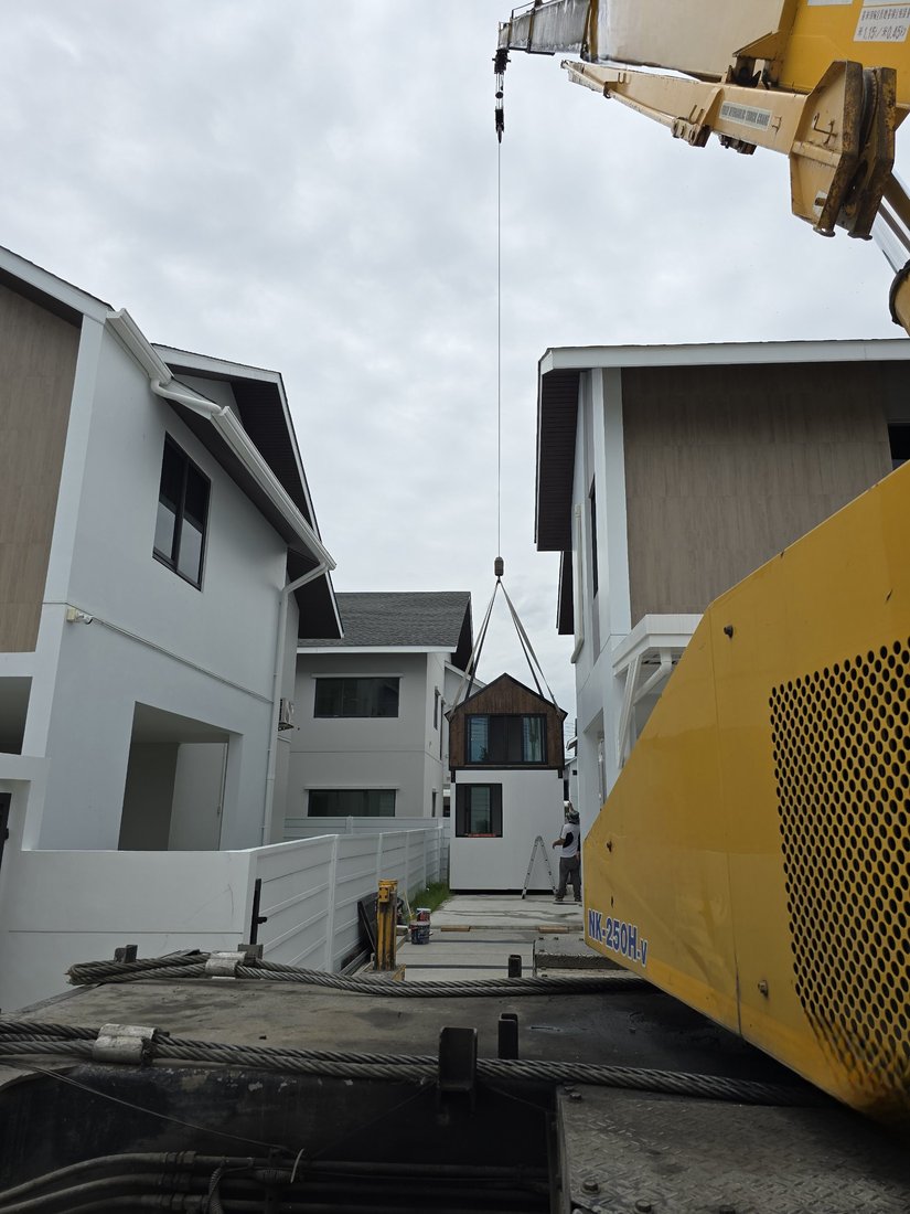 เครนยกบ้านน็อคดาวน์ลอยขึ้นระหว่างตัวบ้านในหมู่บ้าน Nirvana ELEMENT บางนา มีทีมงานคอยประคองด้านล่าง