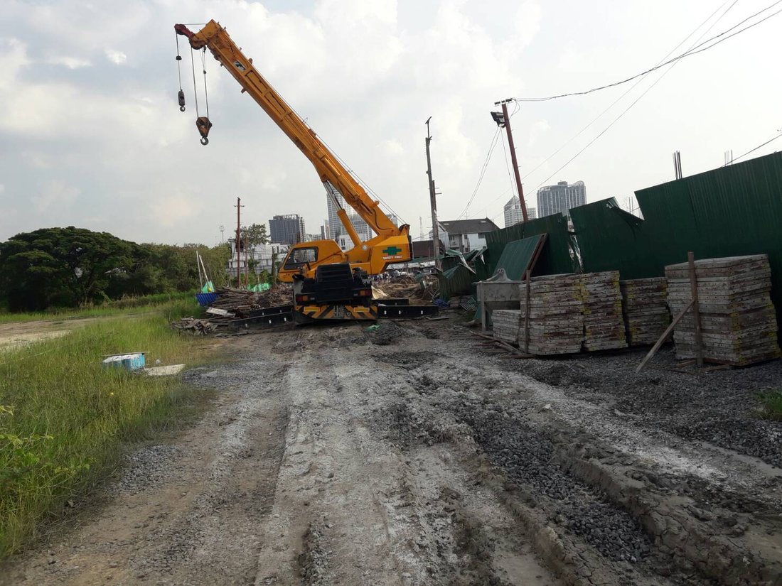 เครนล้อยางสีเหลืองของ BIG MACHINE TRADING ทำงานหน้าไซต์ก่อสร้างบ้านย่านพระโขนง ถนนแคบมีสายไฟฟ้าพาดผ่าน