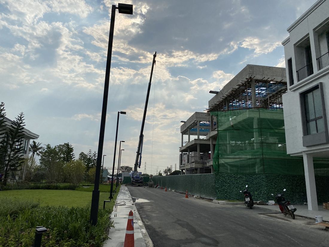 ถนนภายในโครงการหมู่บ้านที่ตกแต่งภูมิทัศน์เสร็จแล้ว เห็นเครนทำงานอยู่ไกลๆ ในส่วนที่ยังก่อสร้างต่อ