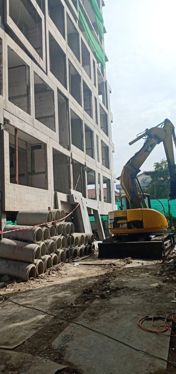 รถขุดตีนตะขาบ CAT 313B ของ BIG MACHINE TRADING ทำงานข้างอาคารก่อสร้างและกองท่อคอนกรีตในไซต์ย่านปุณณวิถี-อุดมสุข