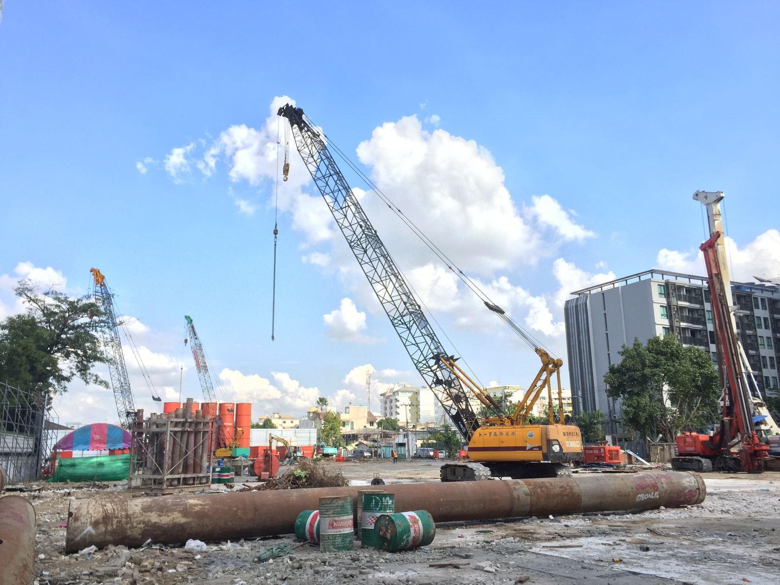 เครนตีนตะขาบเหลือง KOBELCO ของ BIG MACHINE TRADING ทำงานเข็มเจาะเปียก ไซต์งานคอนโดกรุงเทพฯ ท้องฟ้าแจ่มใส