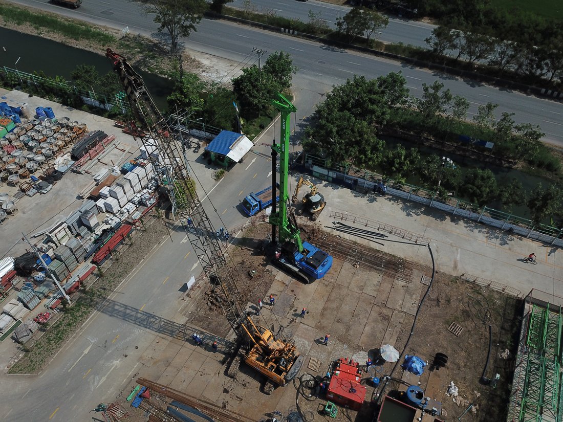 มุมสูงหน้างานฐานรากป้ายบริษัท SYNTEC ถนนบางกรวย-ไทรน้อย มีเครนตีนตะขาบ BIG MACHINE TRADING และรถเจาะเสาเข็มทำงานร่วมกัน