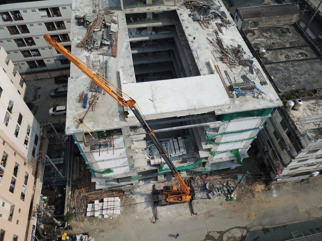 มุมสูงจากโดรน เครนล้อยางทำงานบนดาดฟ้าอาคาร VSK RESIDENCE ถนนกิ่งแก้ว ระหว่างก่อสร้าง มีทีมช่างทำงานอยู่บนอาคาร
