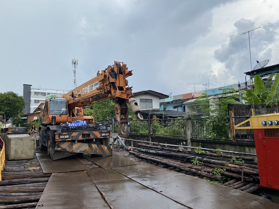 เครนล้อยาง BIG MACHINE TRADING ยกวัสดุบนแท่นเหล็กกลางพื้นที่เปียกแฉะที่ไซต์บ่อบำบัดน้ำเสีย