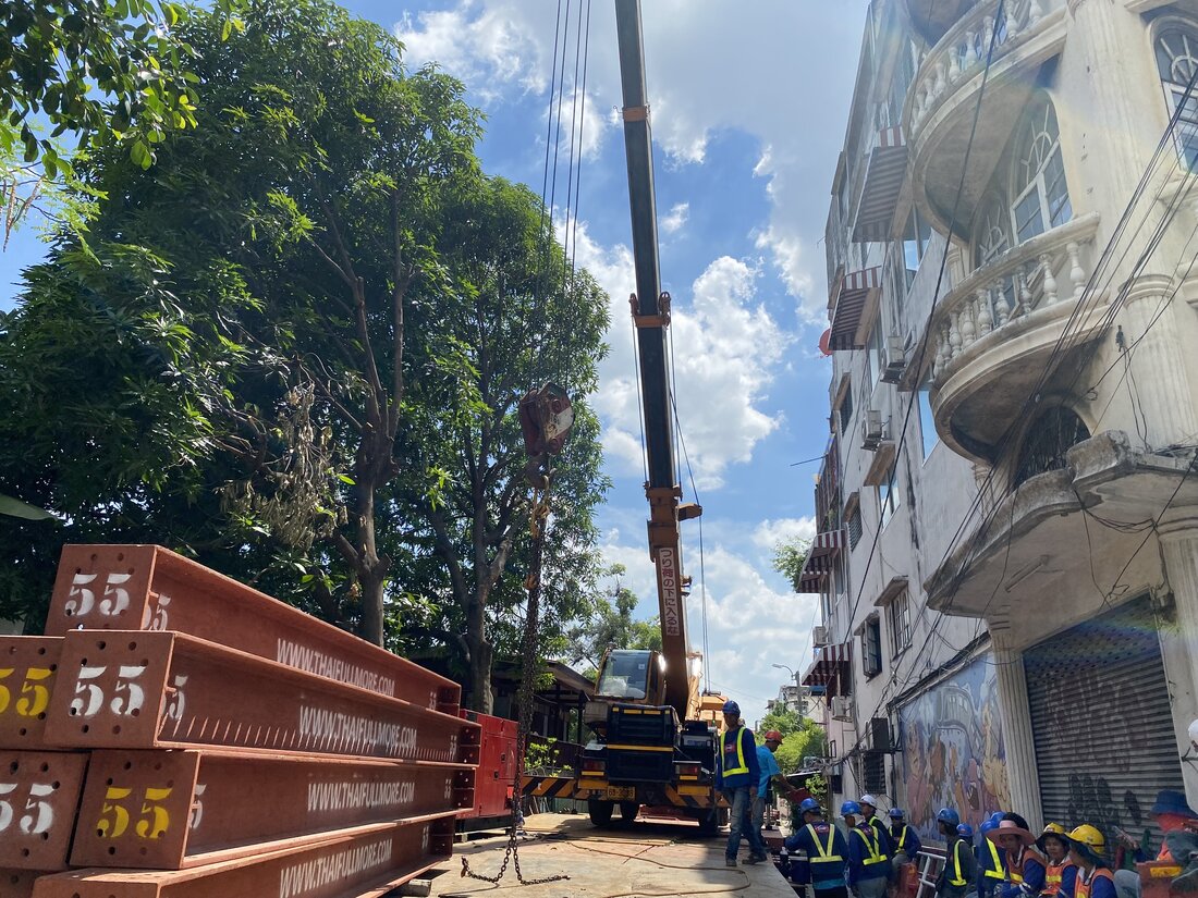 เครนล้อยาง BIG MACHINE TRADING เตรียมยกคานคอนกรีตสำเร็จรูปในตรอกซอยแคบริมคลอง ฝั่งธนบุรี ใกล้อาคารเก่าที่มีระเบียงโบราณ