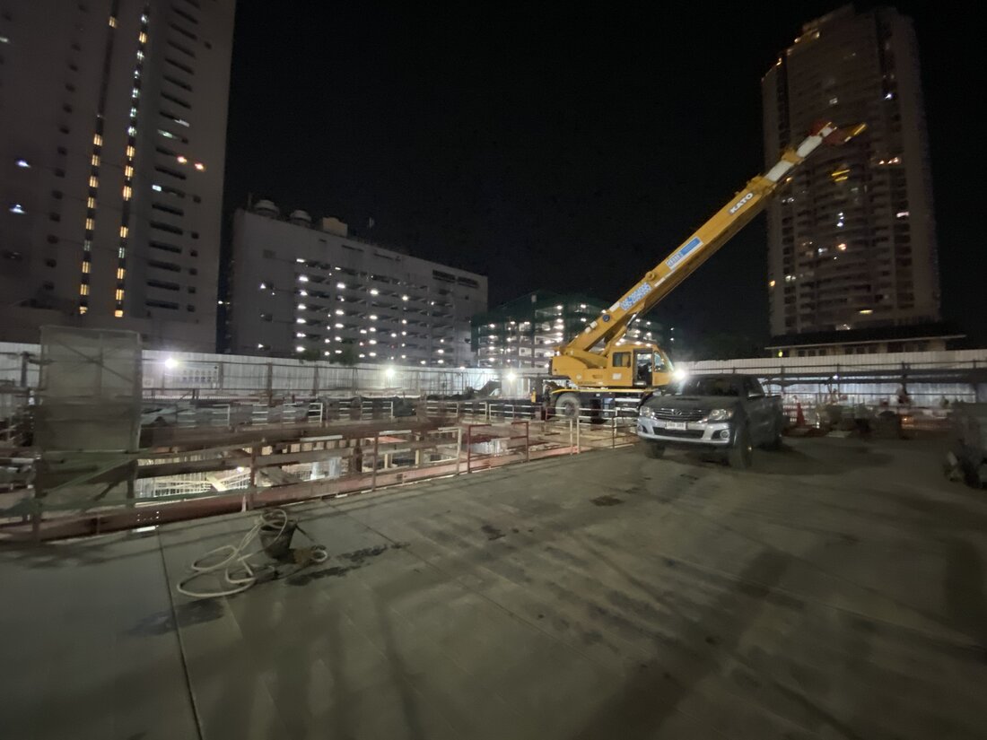 เครนล้อยาง BIG MACHINE TRADING ทำงานกลางคืนที่ไซต์ก่อสร้างโรงพยาบาล ท่ามกลางตึกสูงที่มีแสงไฟโดยรอบ