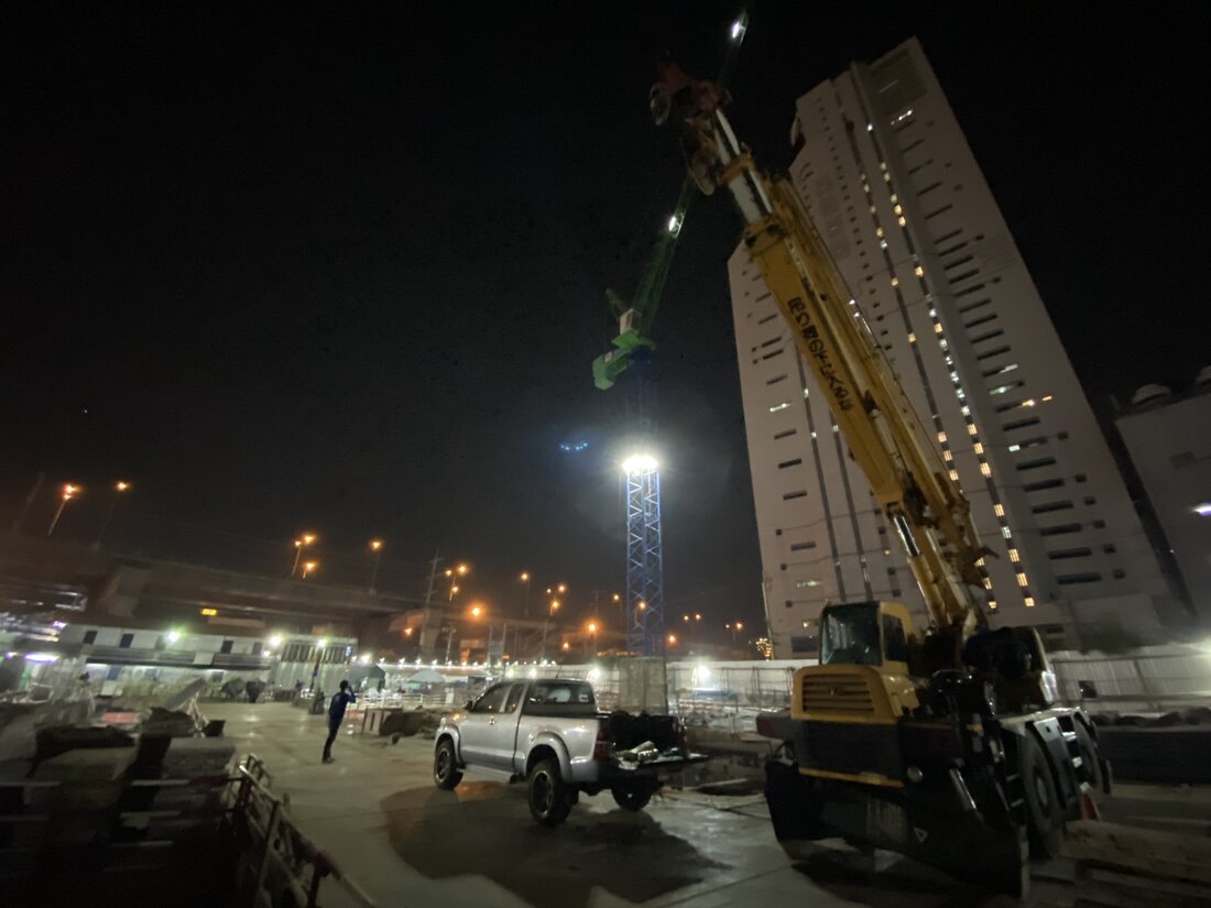 เครนล้อยาง BIG MACHINE TRADING กางบูมทำงานกลางคืน เทียบกับอาคารสูงด้านหลังที่ไซต์ก่อสร้างโรงพยาบาลวัฒนเวชช์ อินเตอร์เนชั่นแนล
