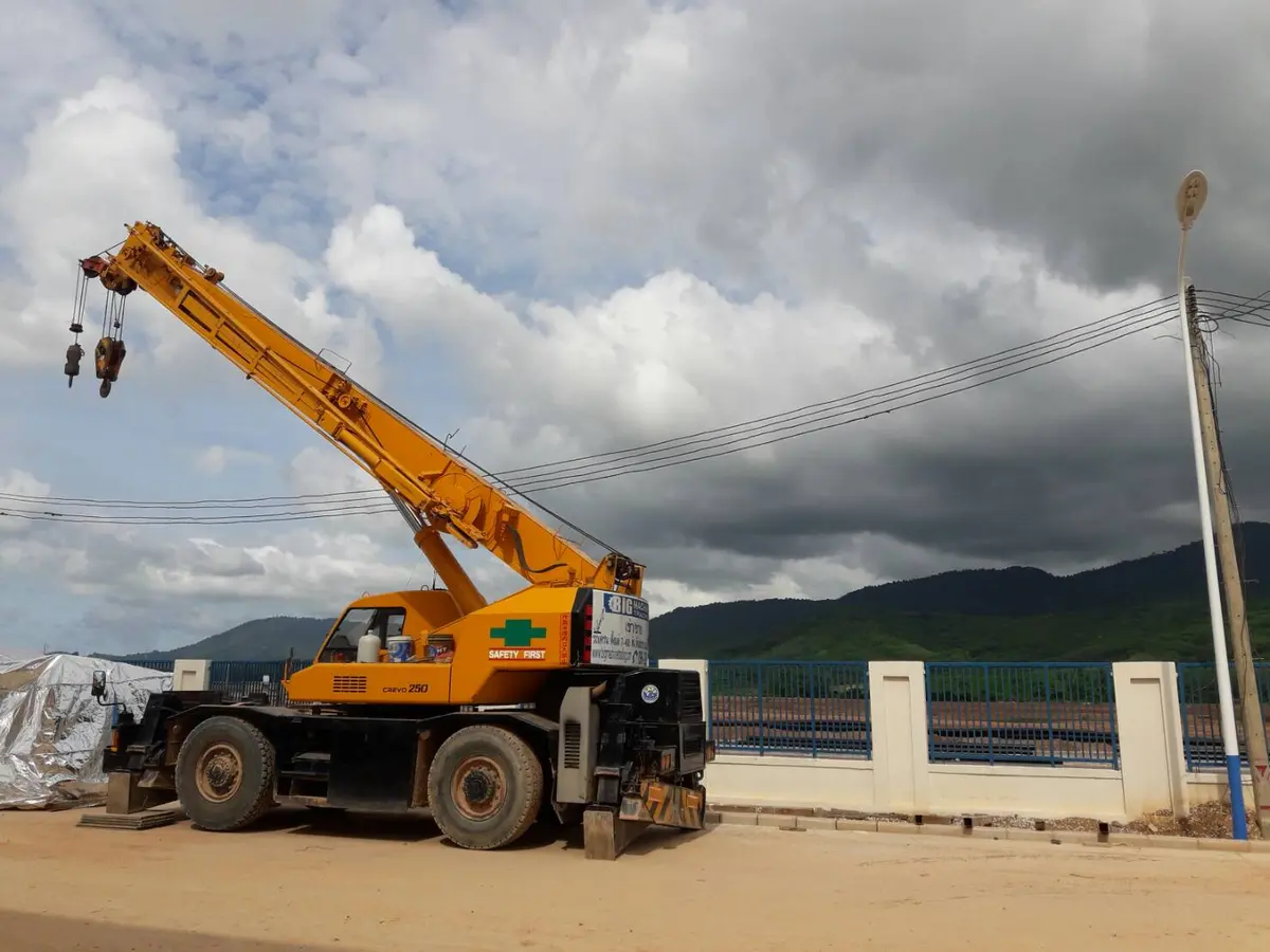 เครน BIG MACHINE TRADING ทำงานริมถนนในระยอง ภูเขาเป็นฉากหลัง